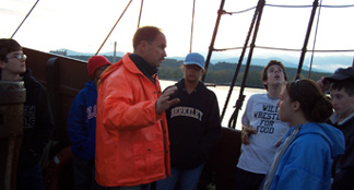 Captain Reynolds holds an anchor watch briefing on the weather deck as the sun sinks low.