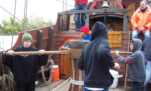 Four students prepare to work the capstan as Captain Reynolds looks on.
