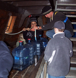 Alex S. and Mr. Dawson fill water bottles on the orlop deck as Nick looks on.