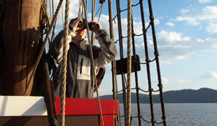 Nick uses binoculars to scan the horizon while looking out from the fore deck.