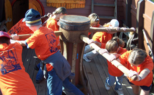 Orange-clad students work the capstan.