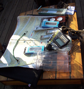 A collection of charts and scientific instruments clustered atop an aft hatch on the weatherdeck often used as a table.