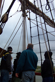 Captain Reynolds shows new crew members several lines running up to a cluster of blocks (pulleys).