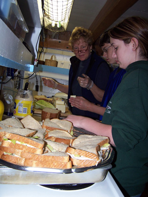 Dylan and Kiera help Mrs. Barton make sandwiches in the galley.