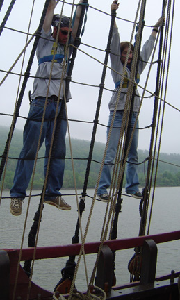 Dr. Dawson and Sam hang by their hands from the rigging above the rail.