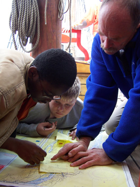 Jamar and Bryan pore over a river chart with Captain Reynolds on the quarter deck.