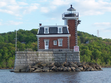 A small red lighthouse sitting on a rocky island at the end of the Athens Channel.