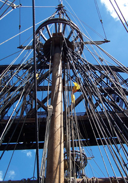 A camera tilts back to see the topmasts and rigging as the ship slides under a bridge.