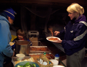 Crew members Arthur Fontikn, Tyler, and Sophia Dijkgraaf serve themselves dinner in the galley.