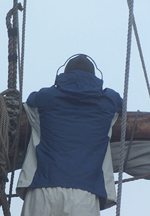 A crew member wears ear protection while standing lookout at the foremast.
