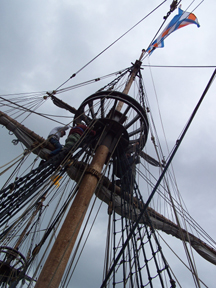 Crew members work aloft on the main mast, with the Dutch tricolor flag fluttering above them.