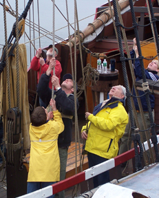 The main mast crew peers skyward as they set the top sail.