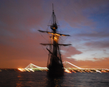 The Half Moon anchored off the Verrazano Narrows Bridge, its anchor light illuminated in the evening gloom.