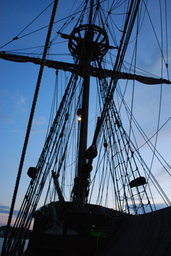 The anchor light hangs from the silhouetted fore mast at dusk.