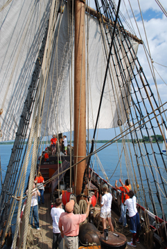 The crew clews up the main course under Captain Reynolds' supervision.