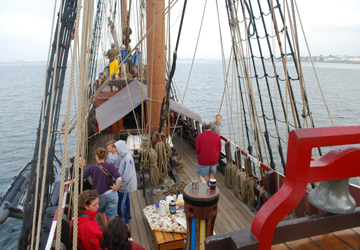 A few crew gather on deck on a hazy morning, with land distantly visible on the horizon.