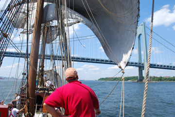 Half of the main course is furled, and half is free as the ship approaches the Verzanno-Narrows Bridge.