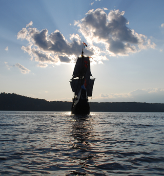 The silhouetted Half Moon is surrounded by a nimbus of light as it sails into the sinking sun.