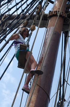Evi hangs in a bosun's chair as she applies wood preservative high on the main mast.