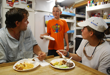 Nick looks on happily as Alex and Sanne eat dinner in the galley.