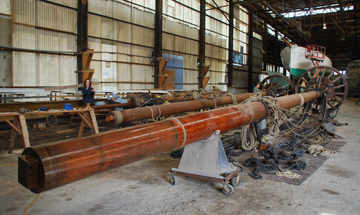 Half Moon crew work on the ship's masts, now lying horizontal in the workshop.