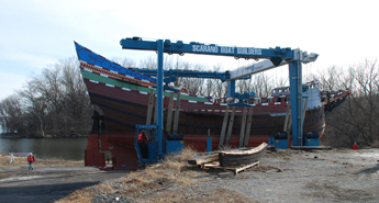 The travelift backs the Half Moon out over a boat launch.