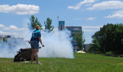 Karen Gilbert fires a cannon with Goodwin College in the background.