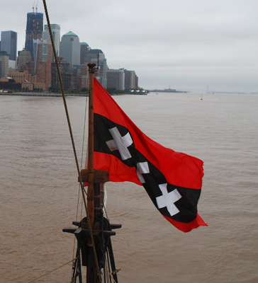 The Amsterdam flag flaps in the wind with lower Manhattan in the background.