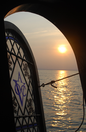 The sun sets over Long Island Sound, seen through the Half Moon's stained glass transom window.